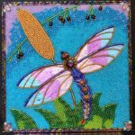 “Glass bead mosaic dragonfly with shimmering pink and blue wings over a bright blue background.”
